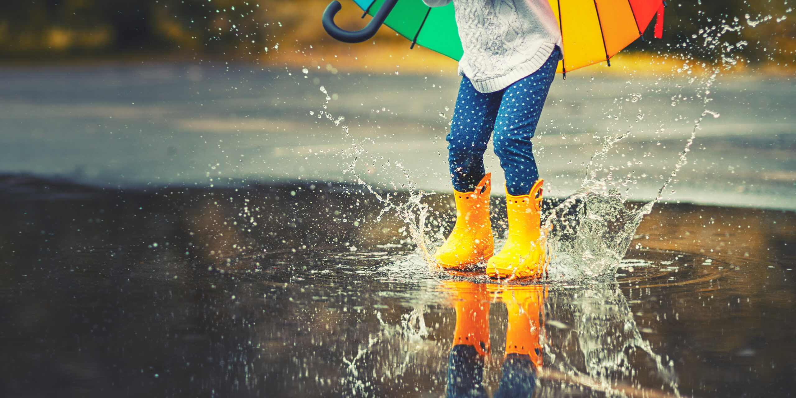 Young child wearing yellow wellies jumping in puddles